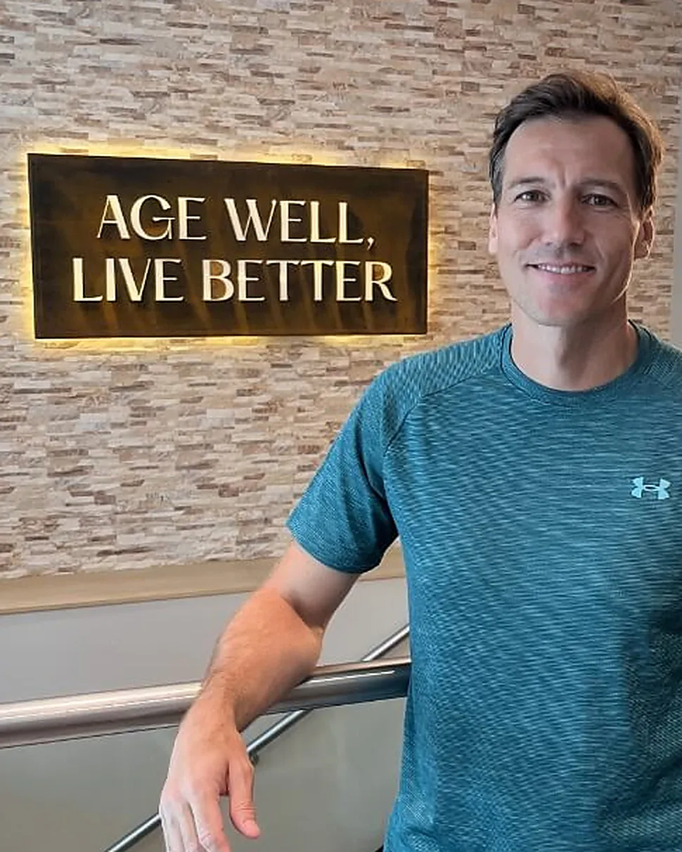 Jonathan at the practice, beside a sign reading Age Well, Live Better
