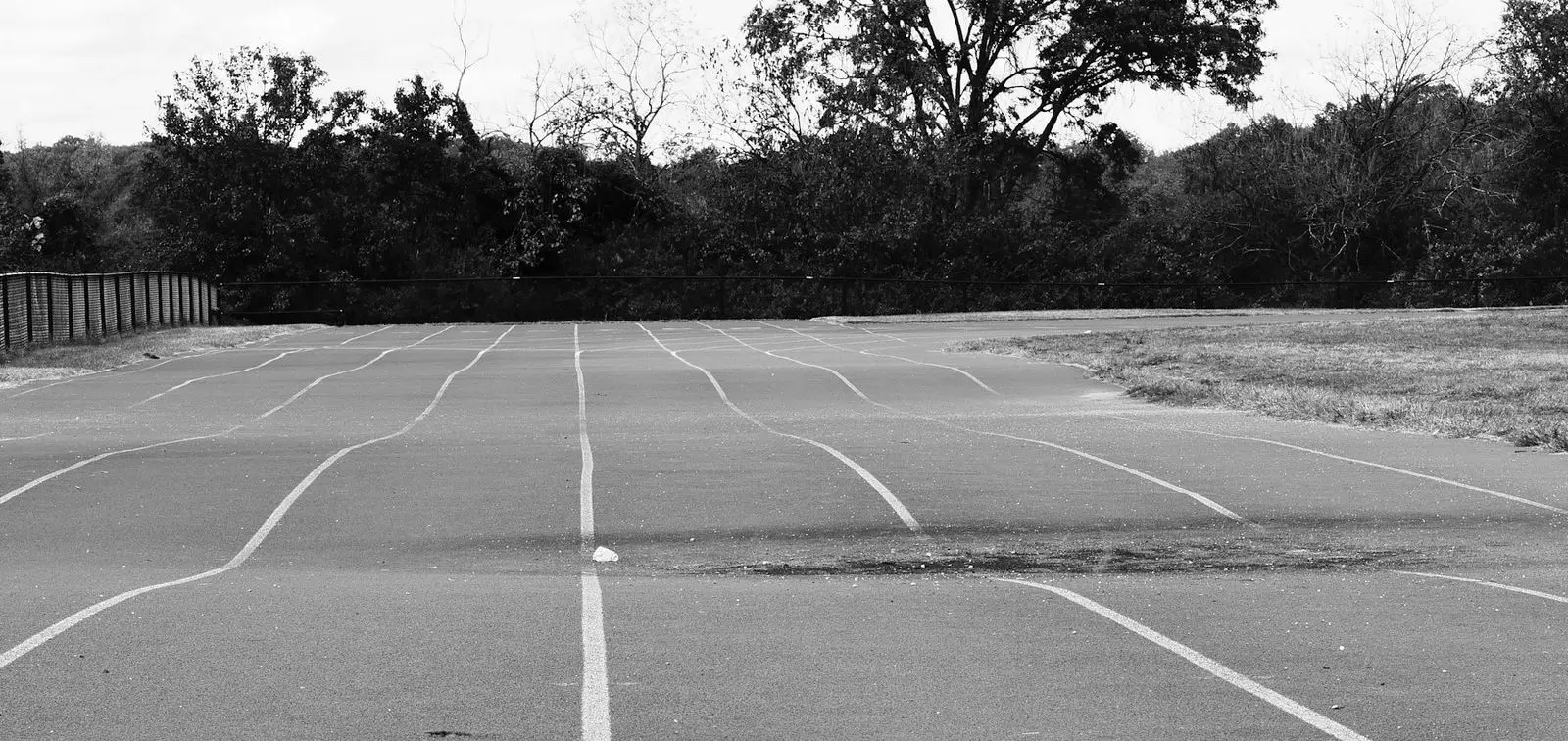 An empty all-weather running track, lanes converging towards a line of trees